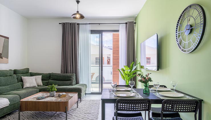 abraj 202 apartment living room with couch tables, chairs,tv and clock with the balcony in the background.